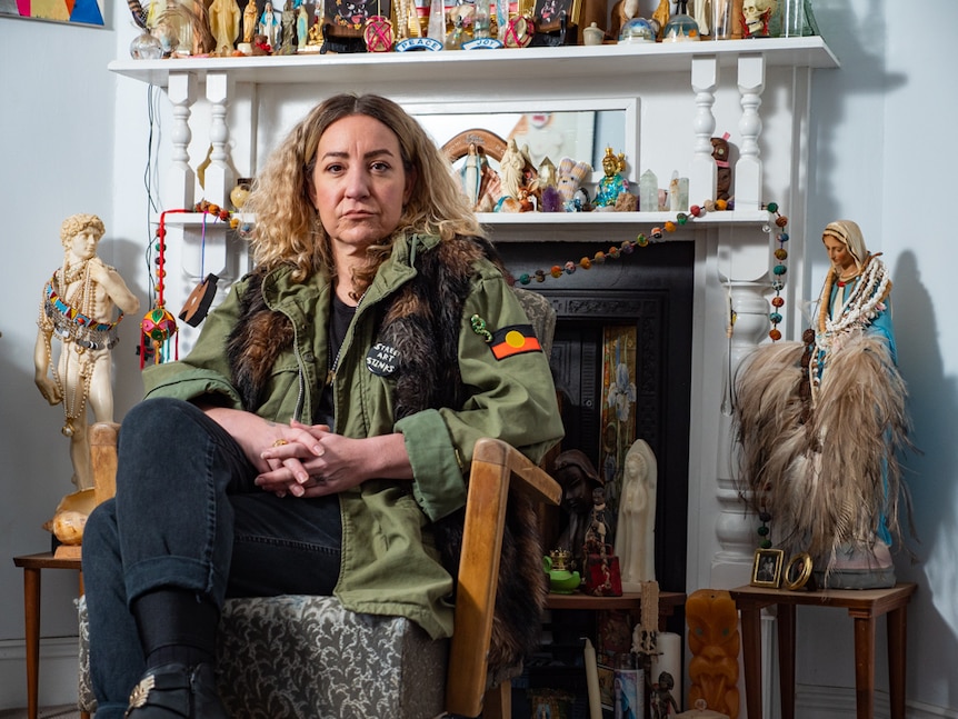 Indigenous artist Amala Bloom sitting in front of mantelpiece display of statuettes.