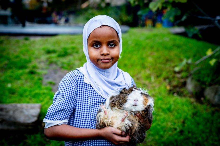 A young girl of African background wearing a headscarf holding a hamster