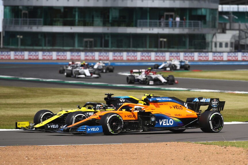 Two Formula One cars are involved in a duel, while several cars are seen behind them in background.