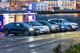 Five electric vehicles parked on a snowy fjord waterfront