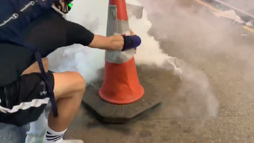 A man covers a billowing tear gas canister with a traffic cone