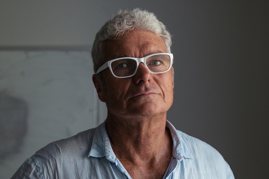 David McBride looks into the camera in a tight closeup portrait. He is wearing glasses and stands in a dark room.