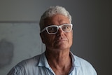 David McBride looks into the camera in a tight closeup portrait. He is wearing glasses and stands in a dark room.