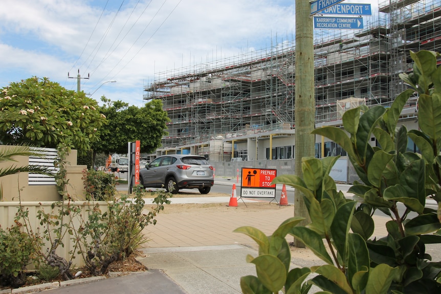 homes and foliage in the foreground, with multi-storey construction site across the road