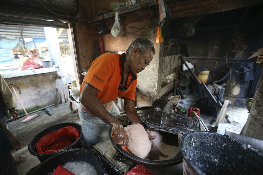 A man processes a pinkened beef mix with his hands in a mixer at an Indonesian market stall.