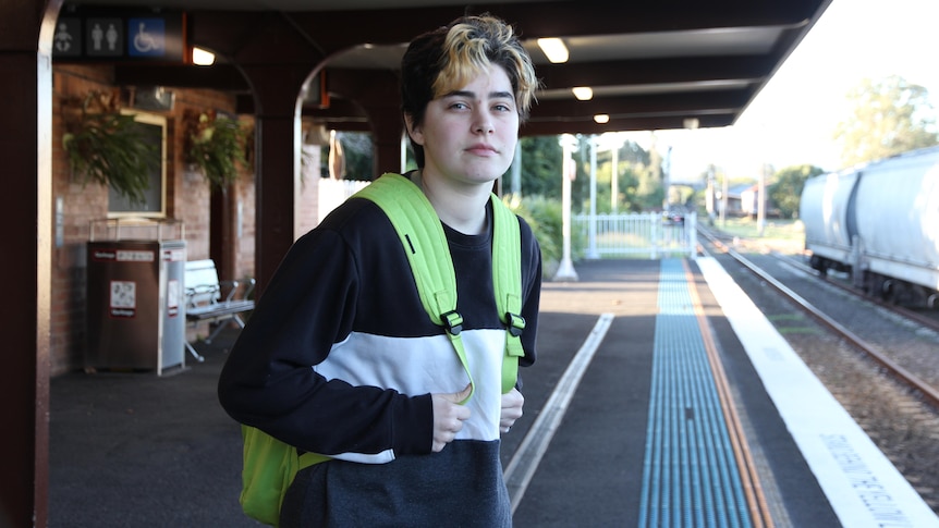 Sage Nikolovski stands holding his back pack and waits for a train on a platform at Wollongong.