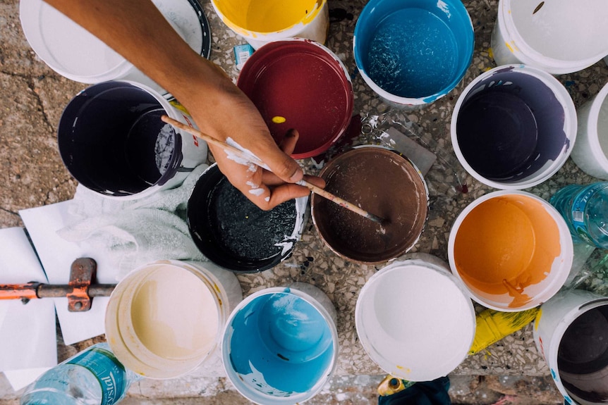 A person's hand dips a paint brush into a paint pot