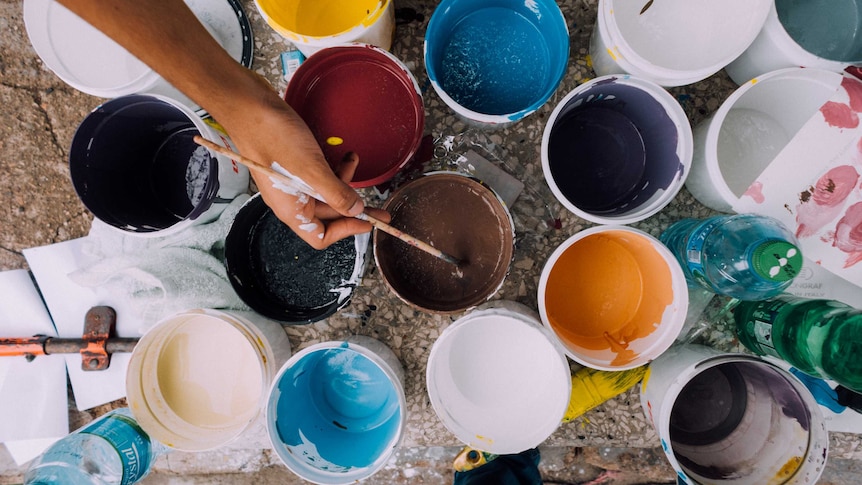 A person's hand dips a paint brush into a paint pot