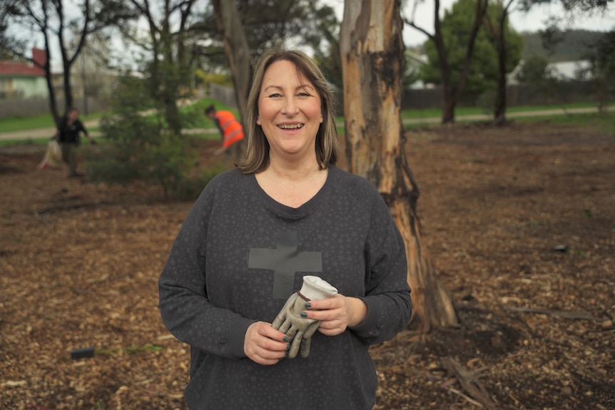 A woman holds gloves in a park and smiles