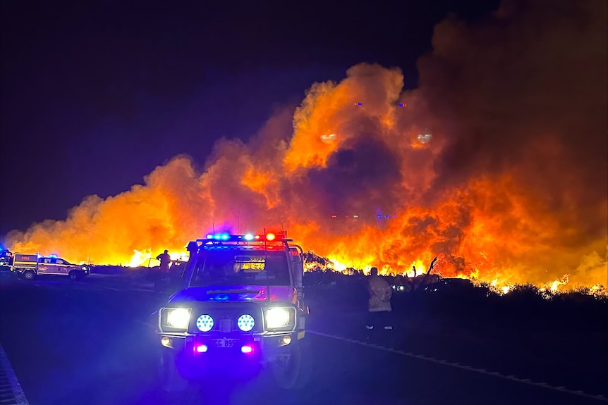Red and blue lights of fire vehicle at night in front of massive smokey blaze. 