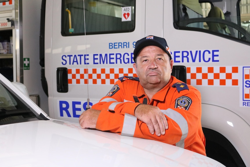 Man in SES uniform leaning on the bonnet of a car, arms folded.