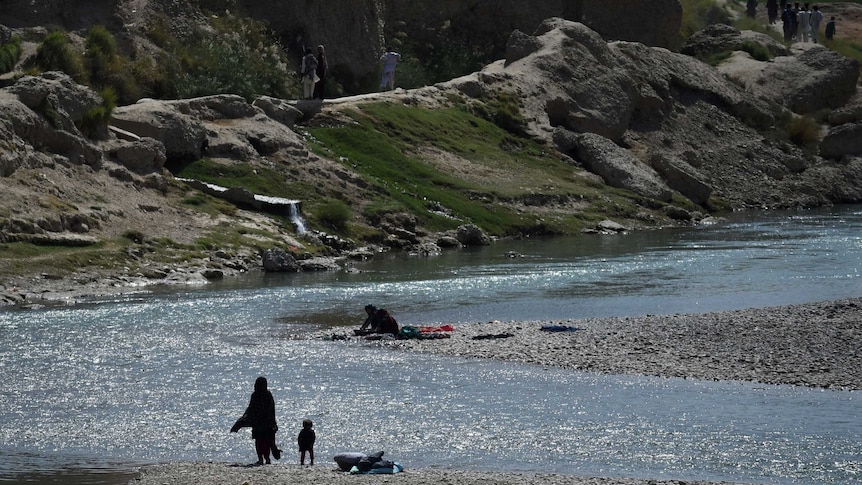 A distant photo of Afghan women washing clothes by a river in Helmand province, as others walk nearby.