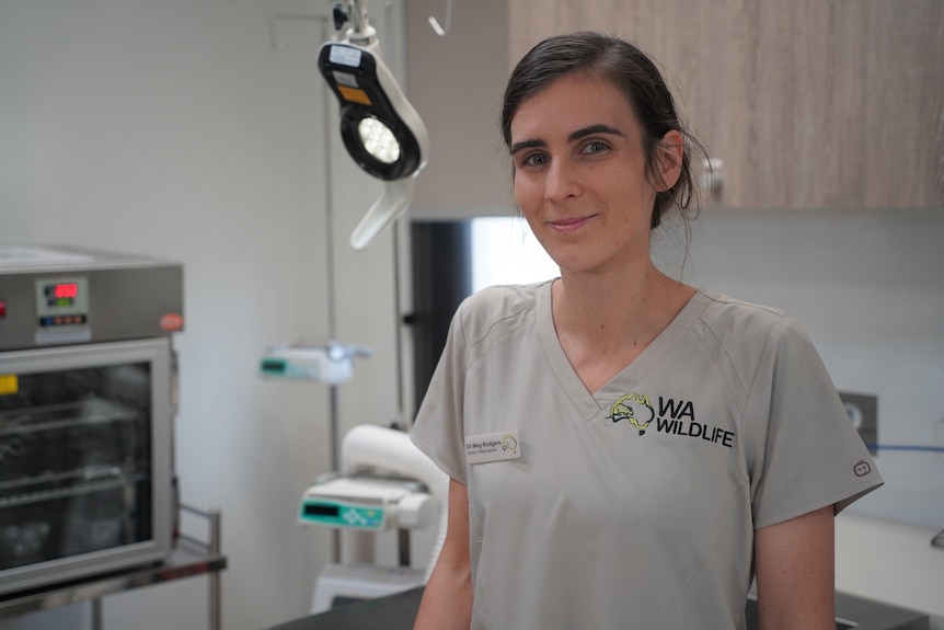 Meg is looking at the camera in her Wildlife WA uniform and name badge and is standing in front of medical equipment.