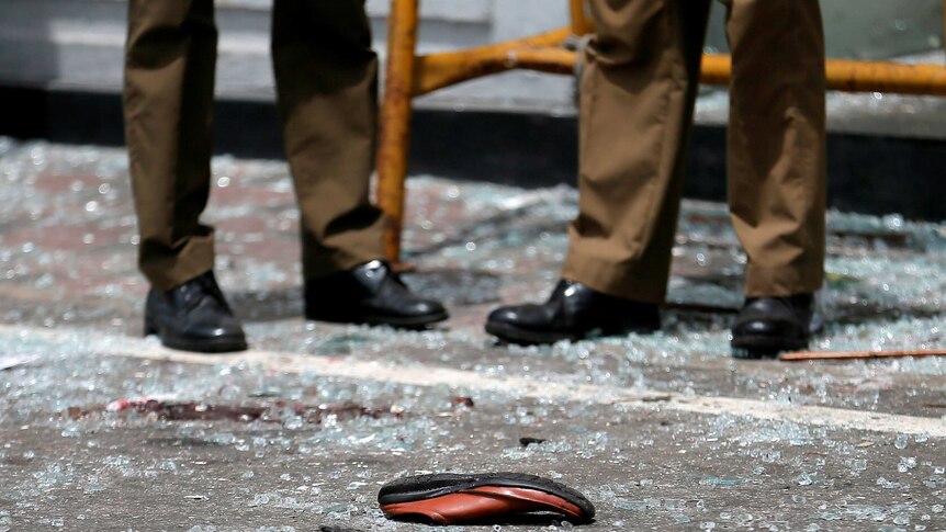 A close up of two military workers' feet on shattered glass, with a single shoe on the ground.