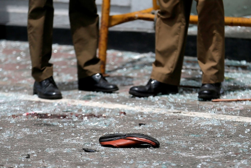 A close up of two military workers' feet on shattered glass, with a single shoe on the ground.