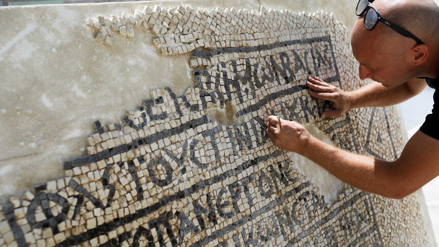 A conservationist cleans a 1,500-year-old mosaic floor bearing Greek writing.
