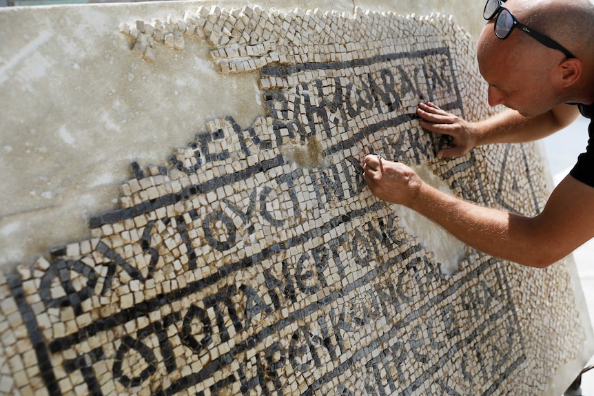 A conservationist cleans a 1,500-year-old mosaic floor bearing Greek writing.