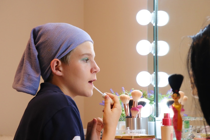 Logan Kelly applies lipstick in the mirror.