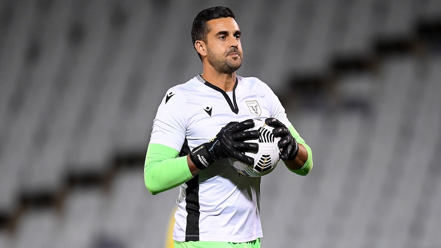 A male goalkeeper holds the ball in two hands prior to an A-League match in the 2020/21 season.
