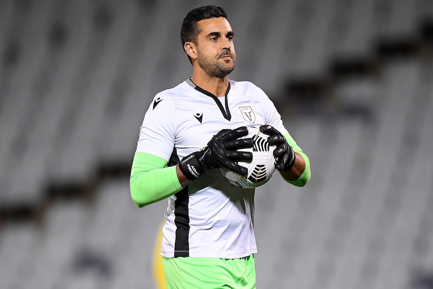 A male goalkeeper holds the ball in two hands prior to an A-League match in the 2020/21 season.