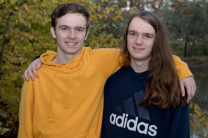 Teo men besides lake with brown and yellow leaves in background, man in yellow jumper with short hair, other long brown hair