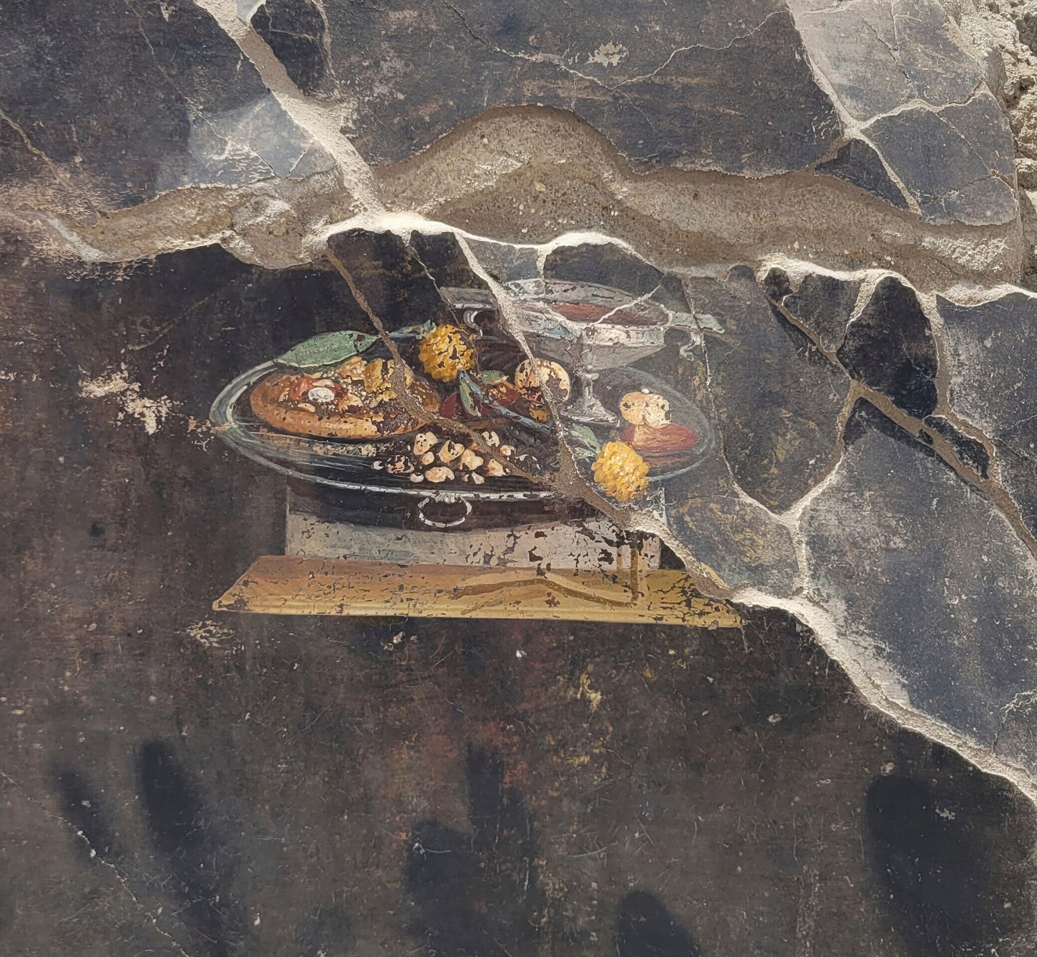 A close-up of a fresco painted on a damaged wall, depicting a table with various foods placed on top of it.