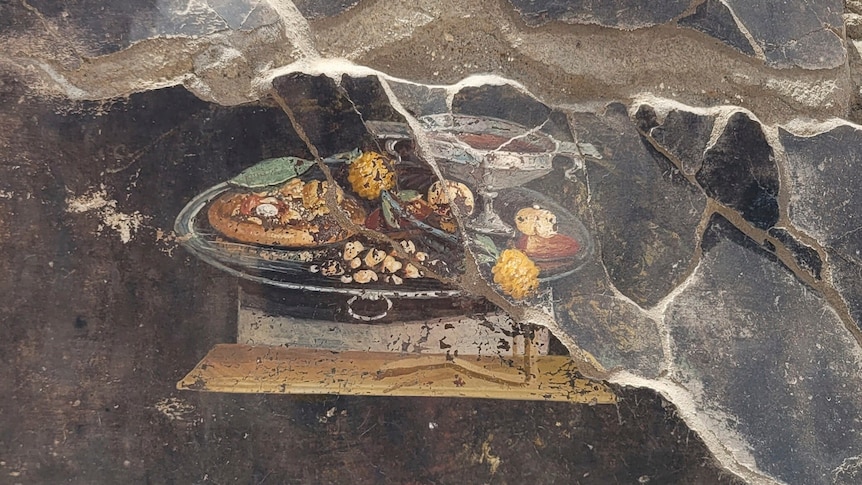 A close-up of a fresco painted on a damaged wall, depicting a table with various foods placed on top of it.