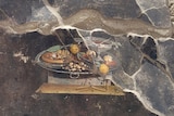 A close-up of a fresco painted on a damaged wall, depicting a table with various foods placed on top of it.