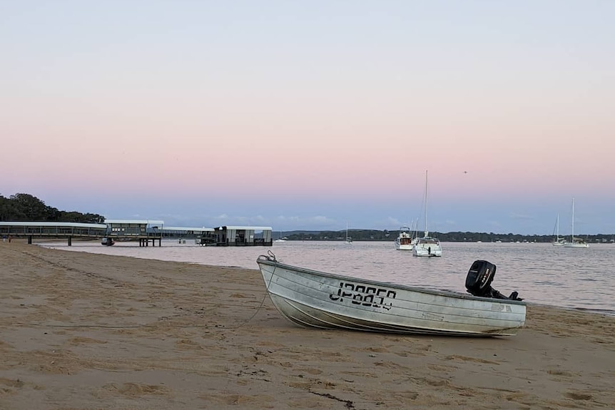 A beach with a small dinghy at the front in sunset.