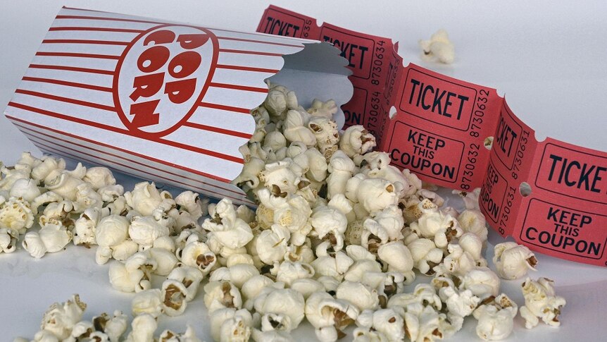 popcorn spilled out of a little popcorn container next to some movie tickets