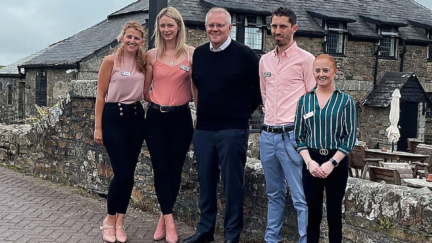 Scott Morrison smiles with four other people outside an old English building with a signpost advertising the Inn. 