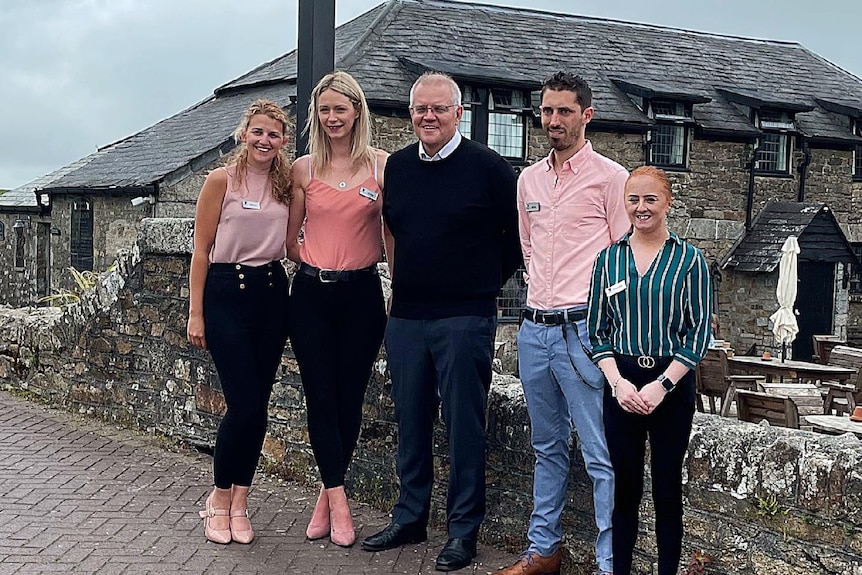 Scott Morrison smiles with four other people outside an old English building with a signpost advertising the Inn. 