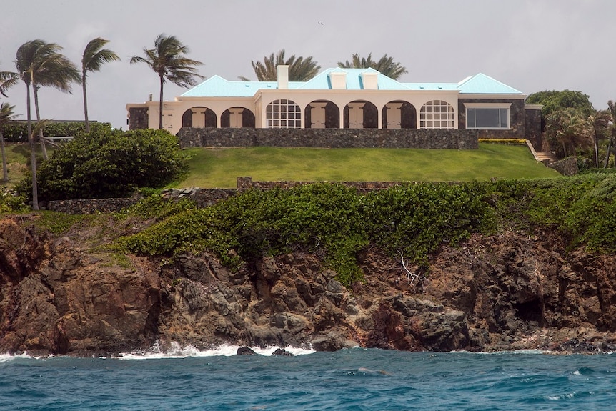 A portion of Jeffrey Epstein's estate on Little Saint James estate, a white facade with palm trees next to the ocean.