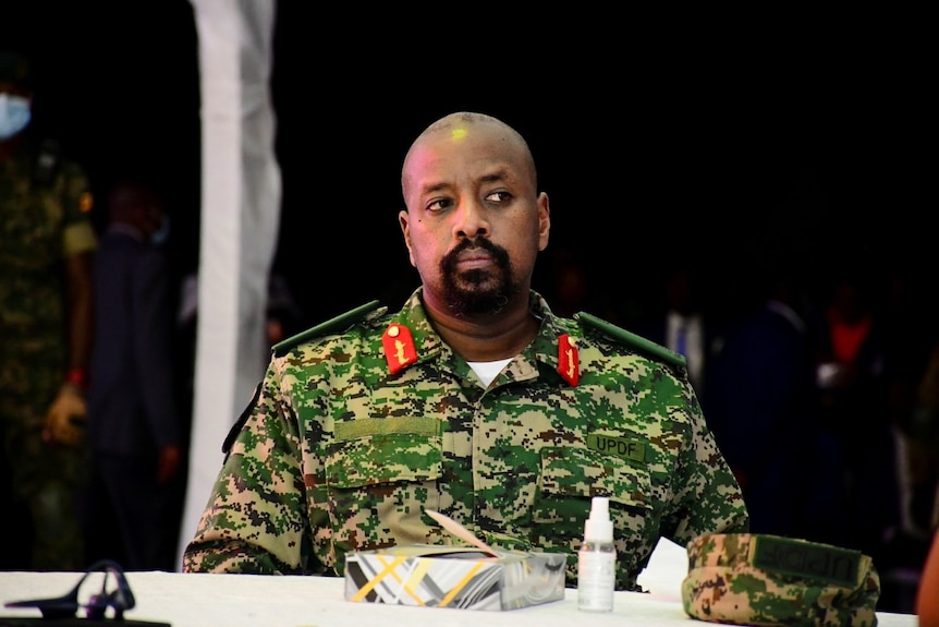 The son of Uganda's president is sitting down at a table wearing a green army uniform