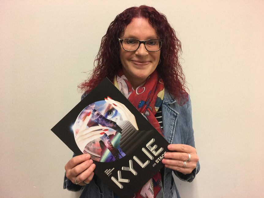 A woman holds the Kylie On Stage exhibition catalogue
