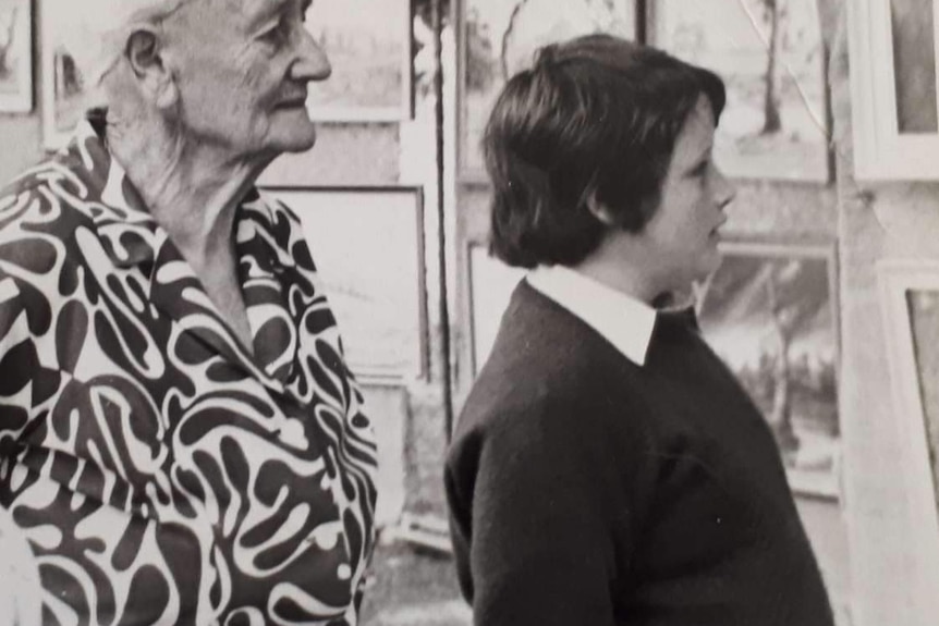 A black and white photo of a young boy standing next to an older women looking at artwork outside.
