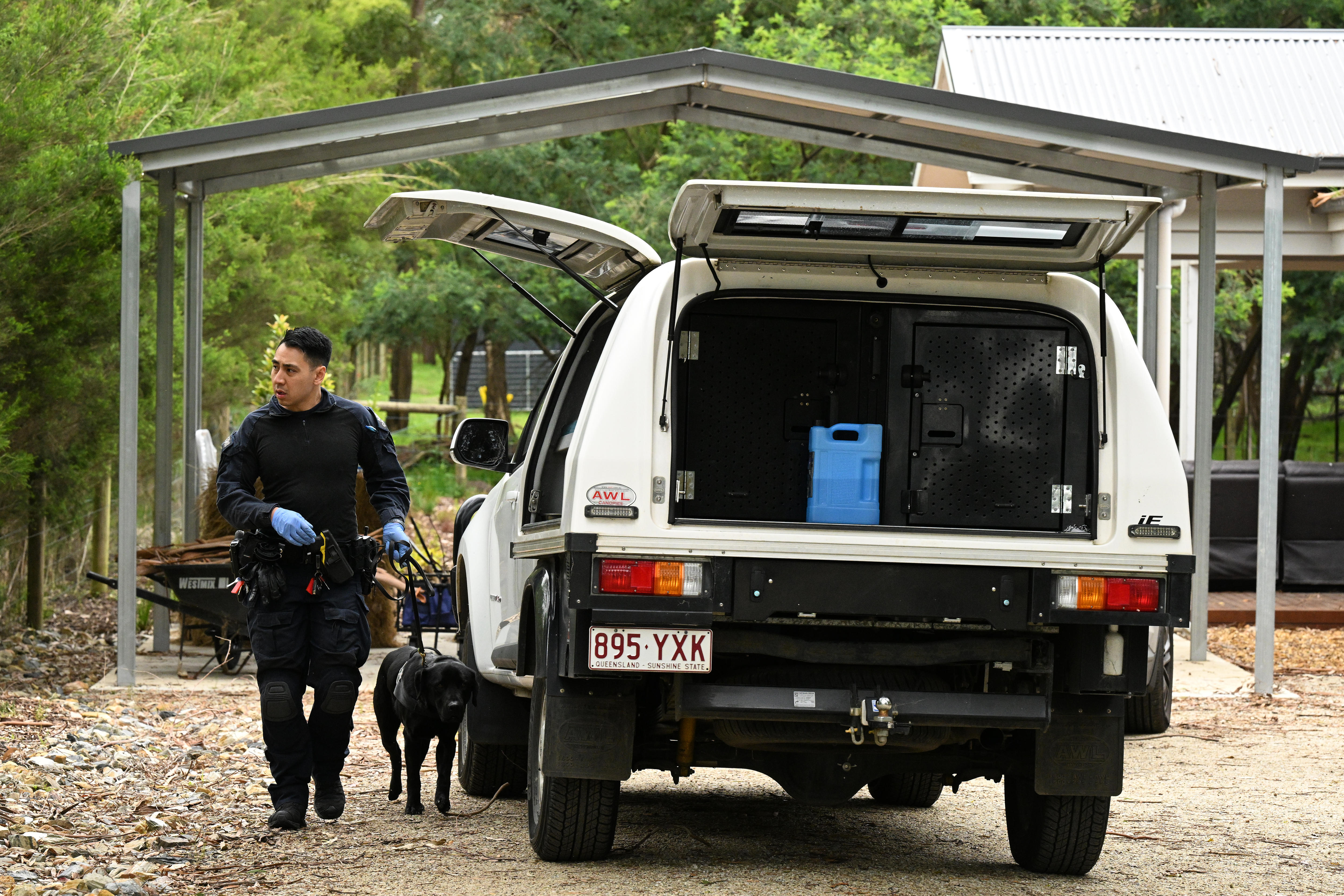 A policeman and police dog next to a police vehicle in a driveway.