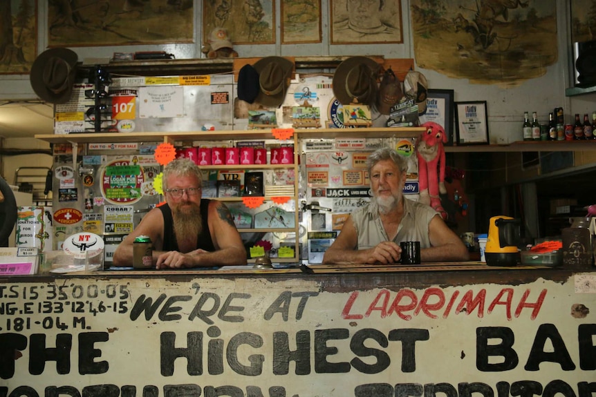 Two men sit behind a bar