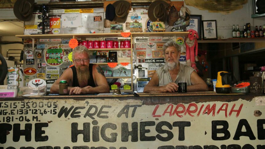 Two men sit behind a bar