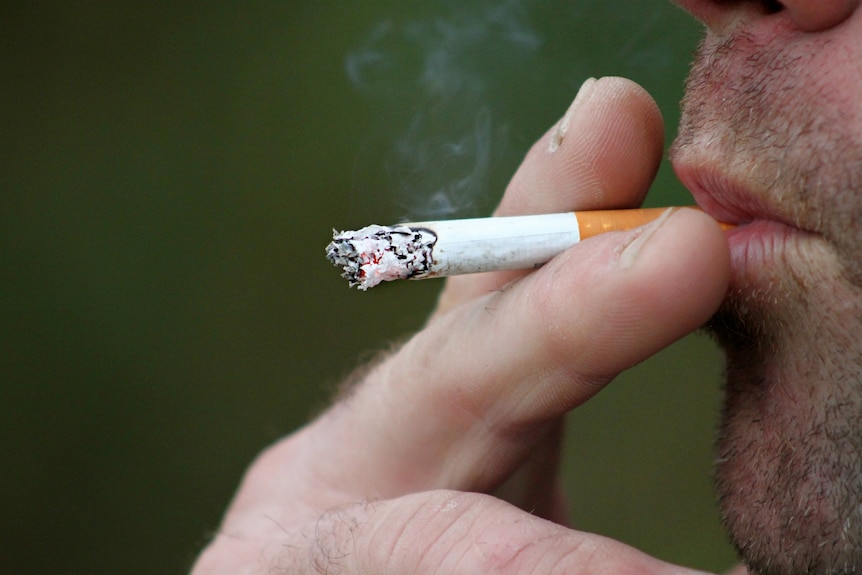 Man inhales cigarette with one hand.