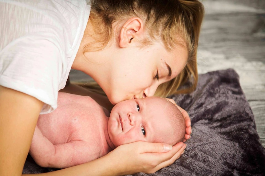 Young woman kissing a very new baby who's lying on a blanket