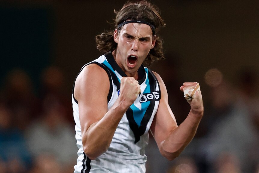 A Port Adelaide AFL player stands with fists clenched, roaring in celebration after a goal in a final.