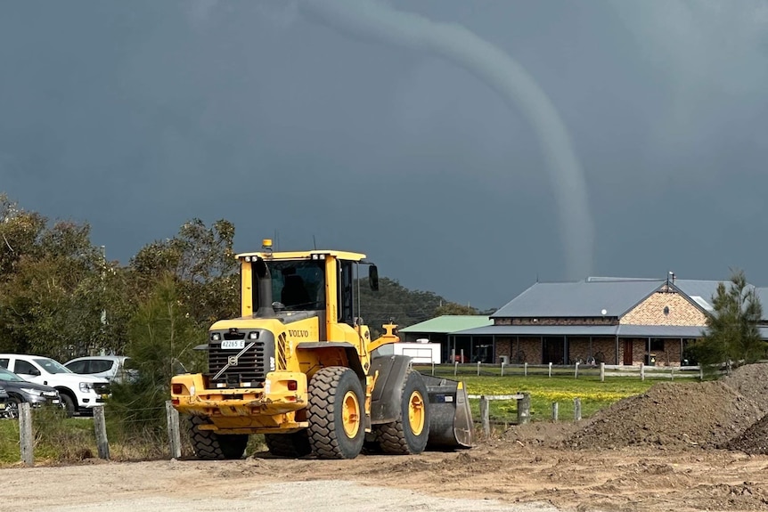 Water spout forms behind a house and yellow tractor