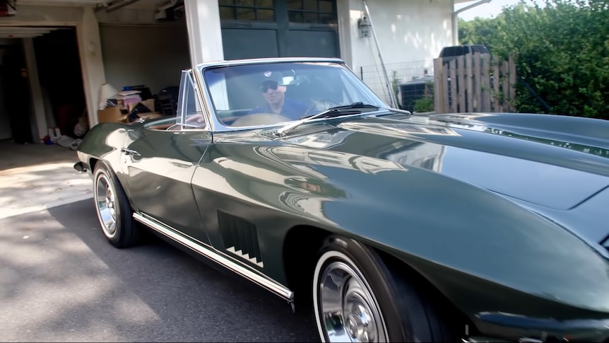 Joe Biden smiles behind the wheel of a green convertible, behind him is an open garage with a cardboard box of papers in it