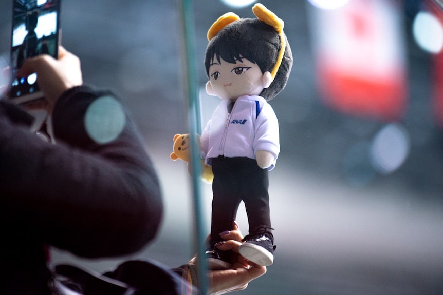 A plush toy of the figure skater Yuzuru Hanyu is held up and photographed.