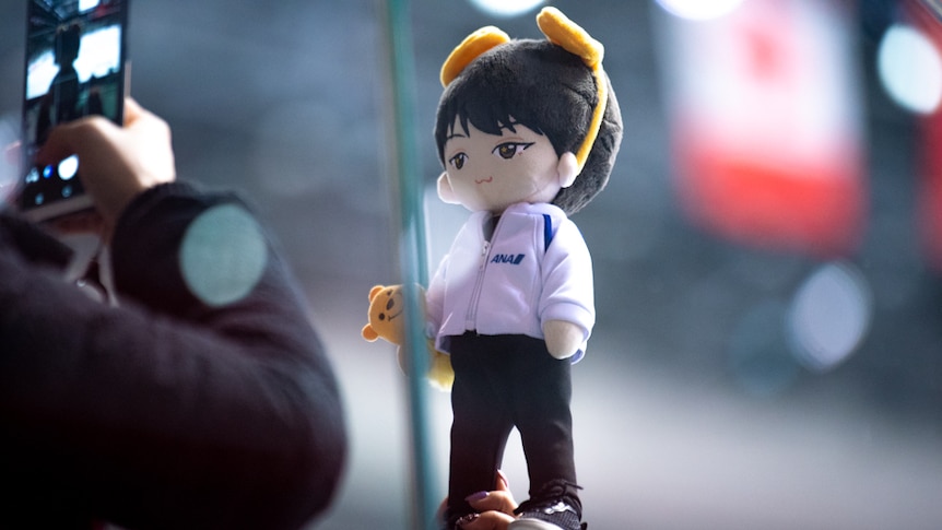 A plush toy of the figure skater Yuzuru Hanyu is held up and photographed.