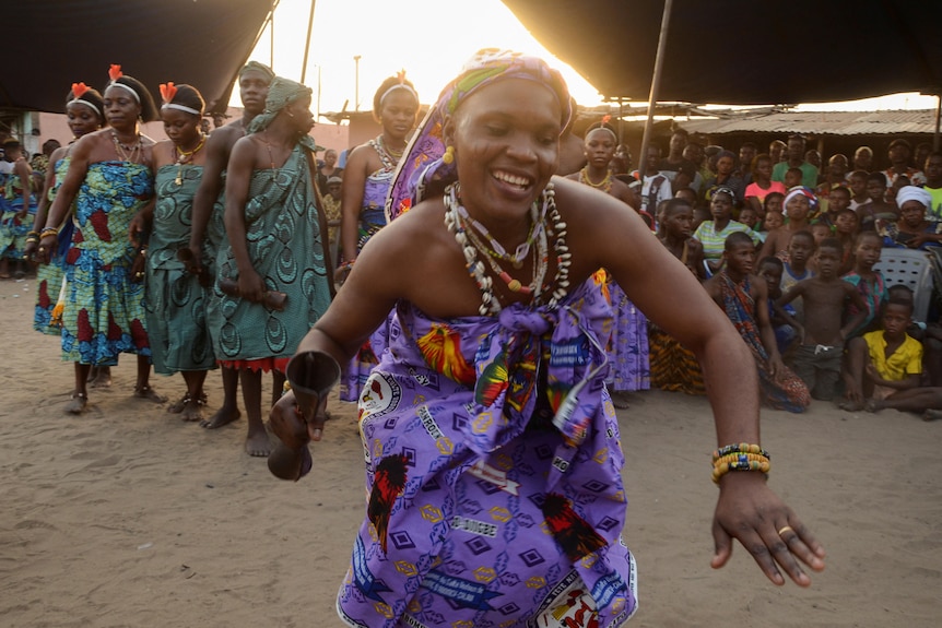 An African woman wearing purple dancing in front of a crowd