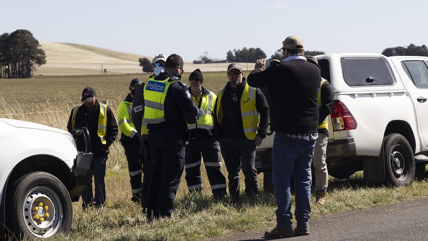 A group of police and contractors on a country road.
