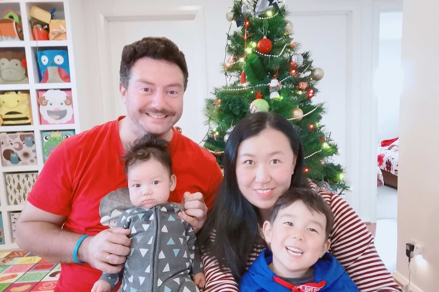 Andrew Bamford, his wife and two young children in front of a Christmas tree.