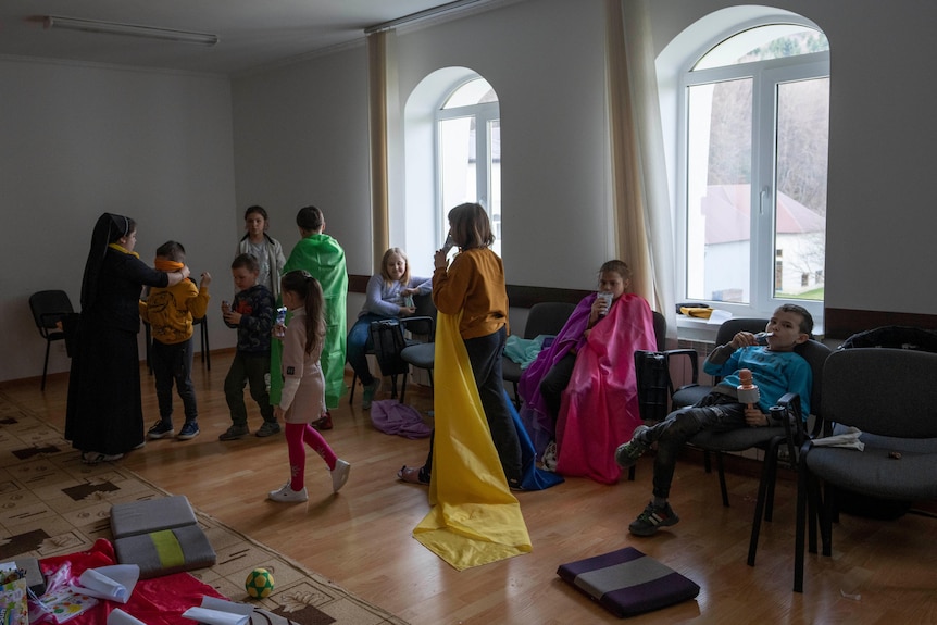 Children wearing colourful clothing playing a game with a nun in a large room.